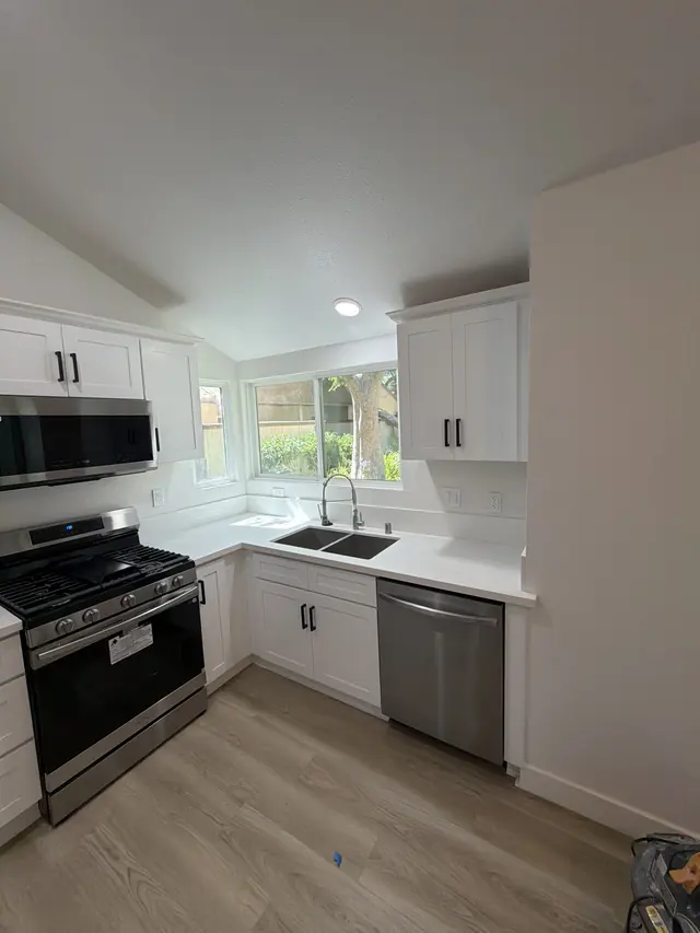 White shaker kitchen with corner windows over the sink and recessed lighting